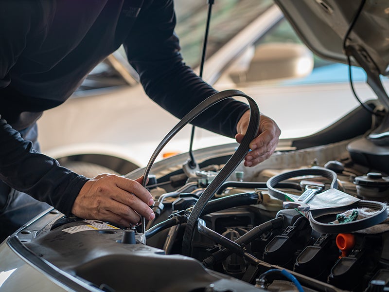 a service tech working on a belt in a vehicle